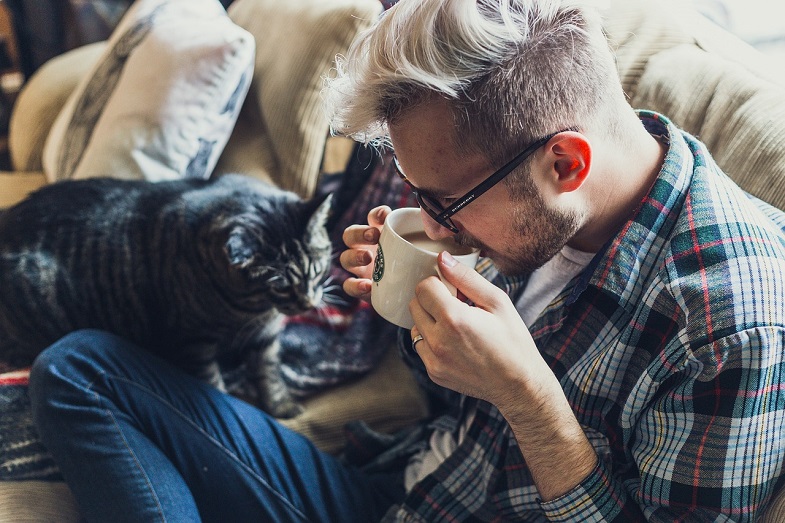 Man drinking coffee in company of cat